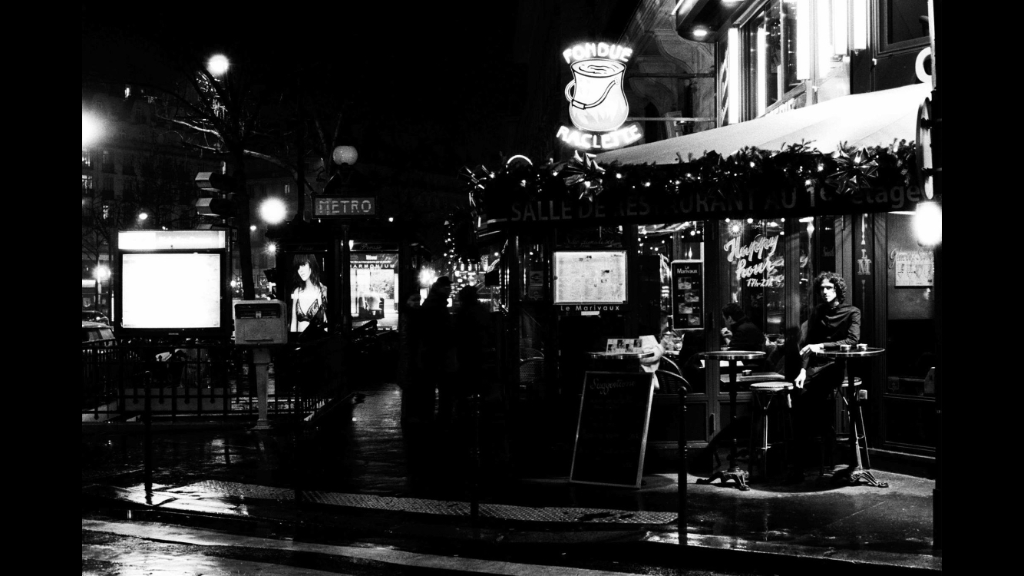 Scène de rue parisienne vintage en noir et blanc avec terrasse de café illuminée