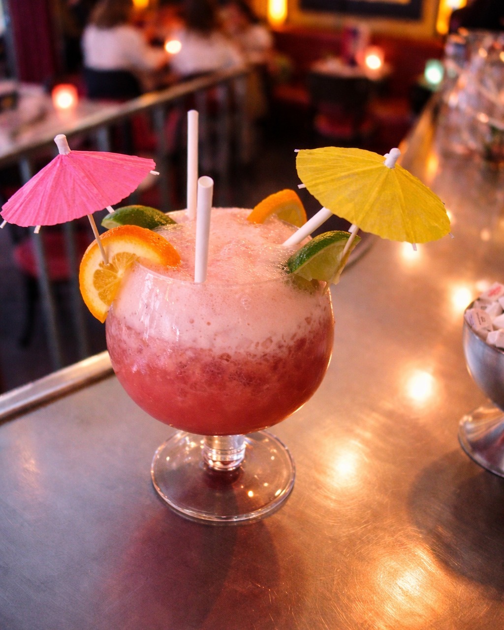 Cocktail tropical rose avec parapluies colorés, glaçons, tranche d'orange et menthe