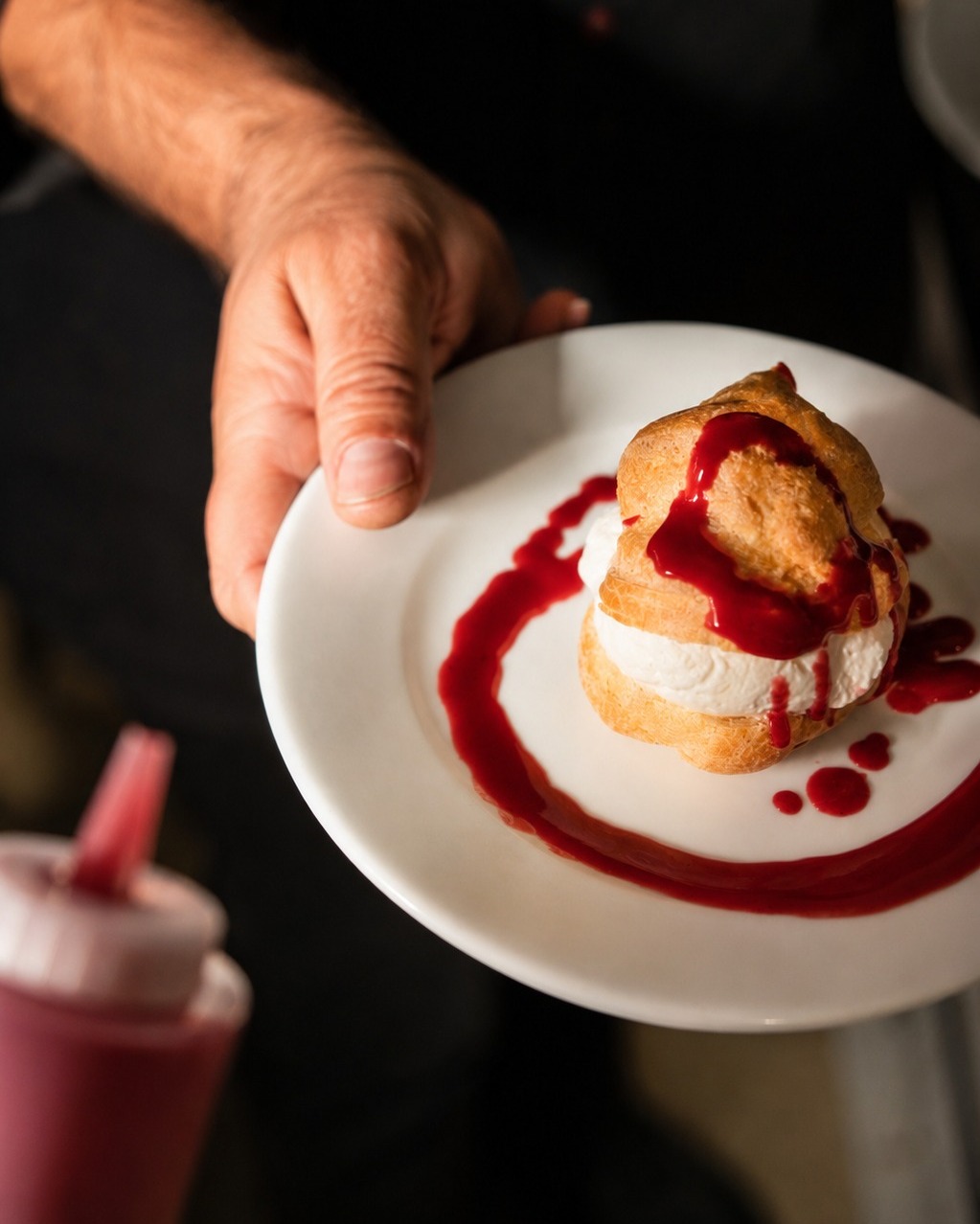 Profiterole garnie de crème et sauce fruits rouges présentée par un chef