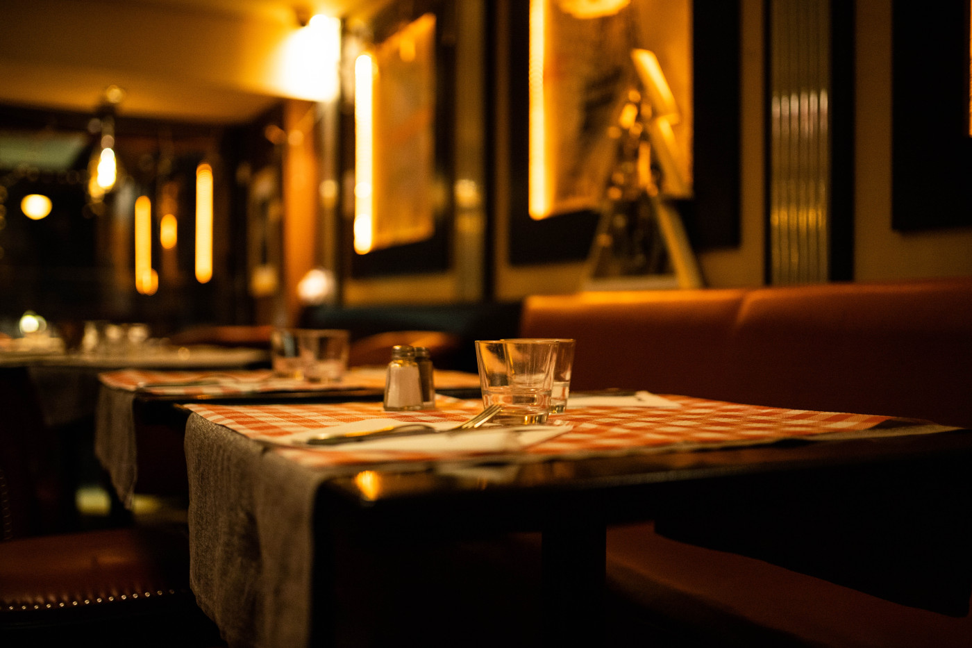 Salle de restaurant élégante éclairée à la lumière chaude avec tables dressées et banquettes
