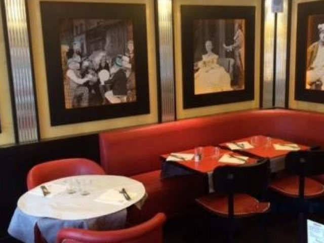 Salle de restaurant élégante avec banquettes rouges, tables noires et tableaux encadrés